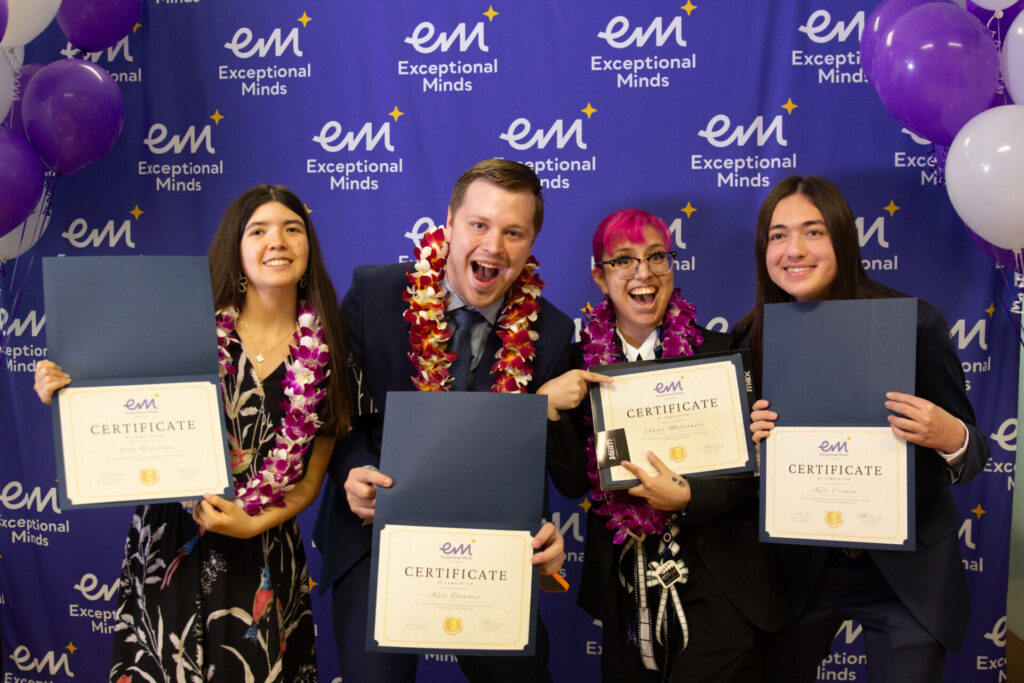 Four students hold up diplomas at their graduation ceremony. 